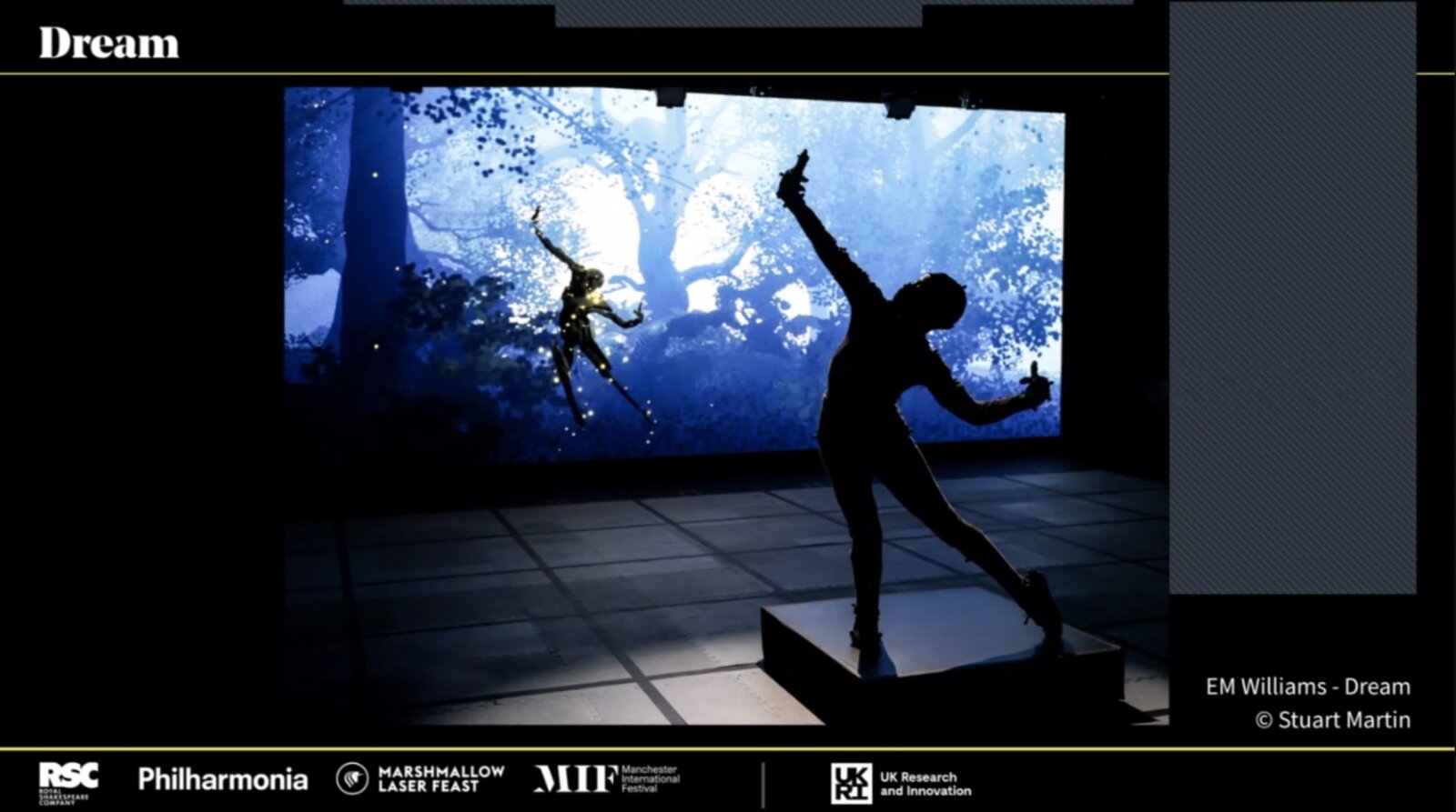 Silhouetted Dream performer in motion capture rig dancing before a screen of a glowing virtual forest with a fairy figure